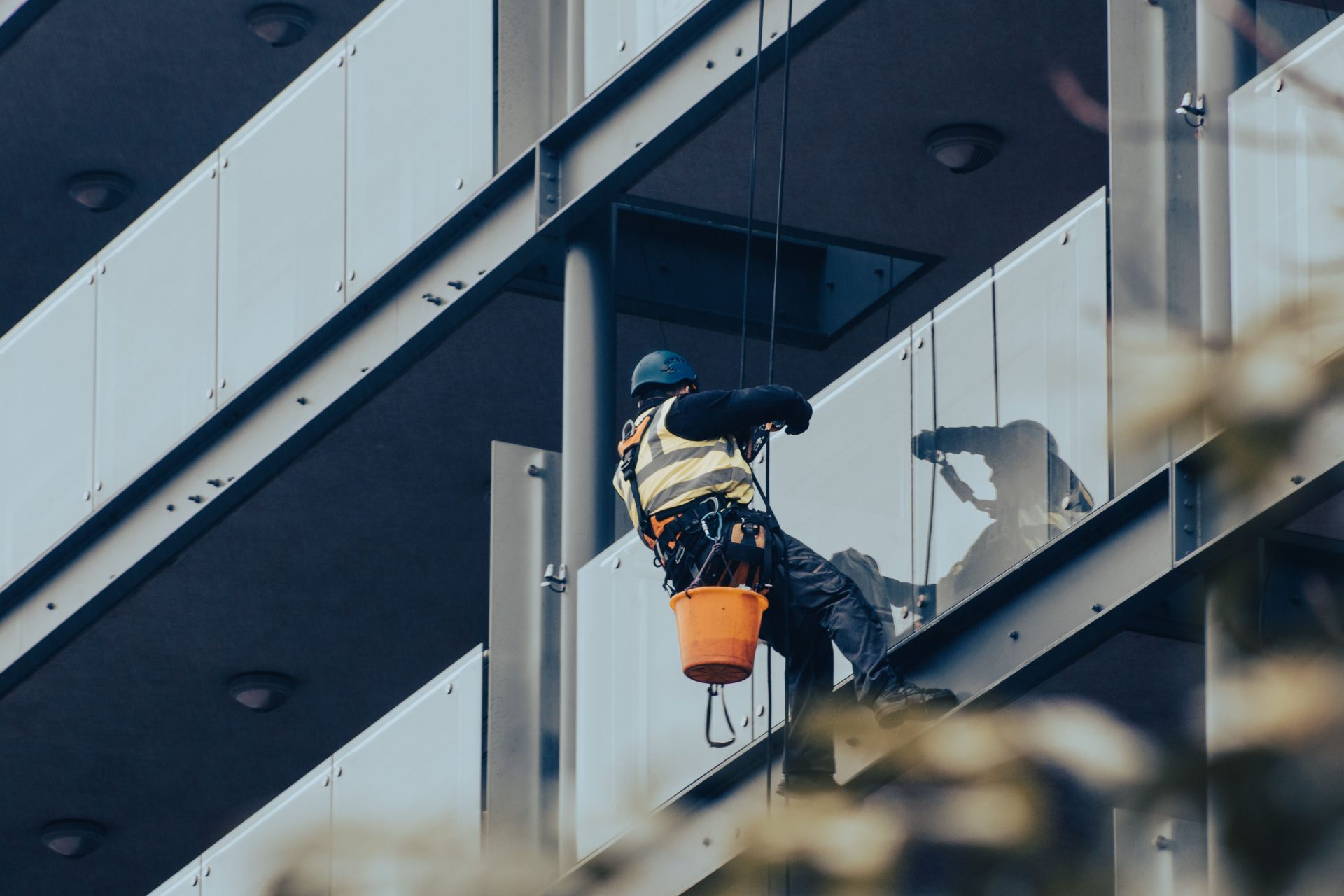 Hochhaus-Fensterputzer bei der Arbeit mit Sicherheitsausrüstung an einer modernen Gebäudefassade.