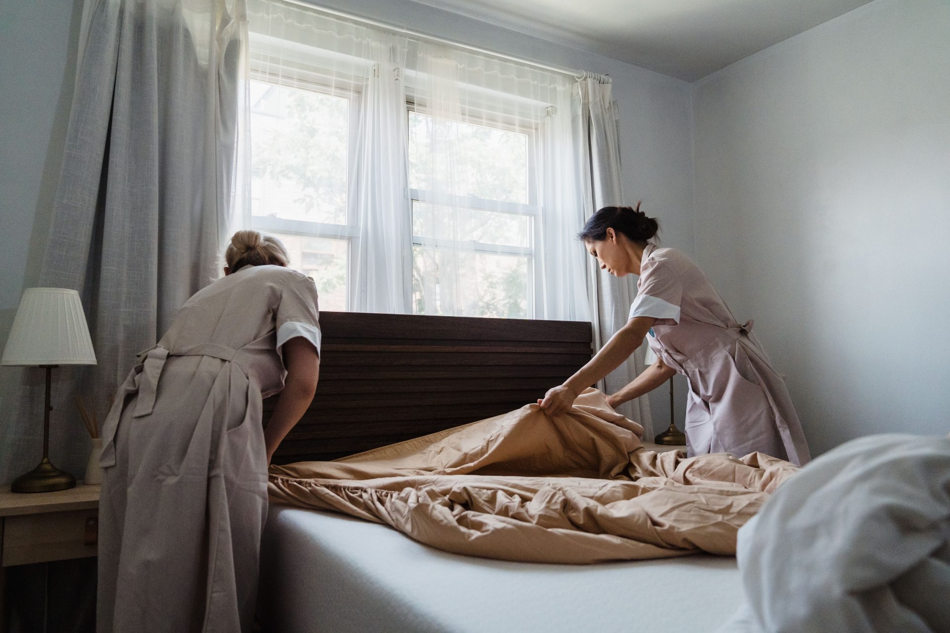 Zwei Zimmerfrauen beziehen ein Bett in einem sonnendurchfluteten Schlafzimmer – ein Bild, das Sauberkeit und Liebe zum Detail vermittelt.