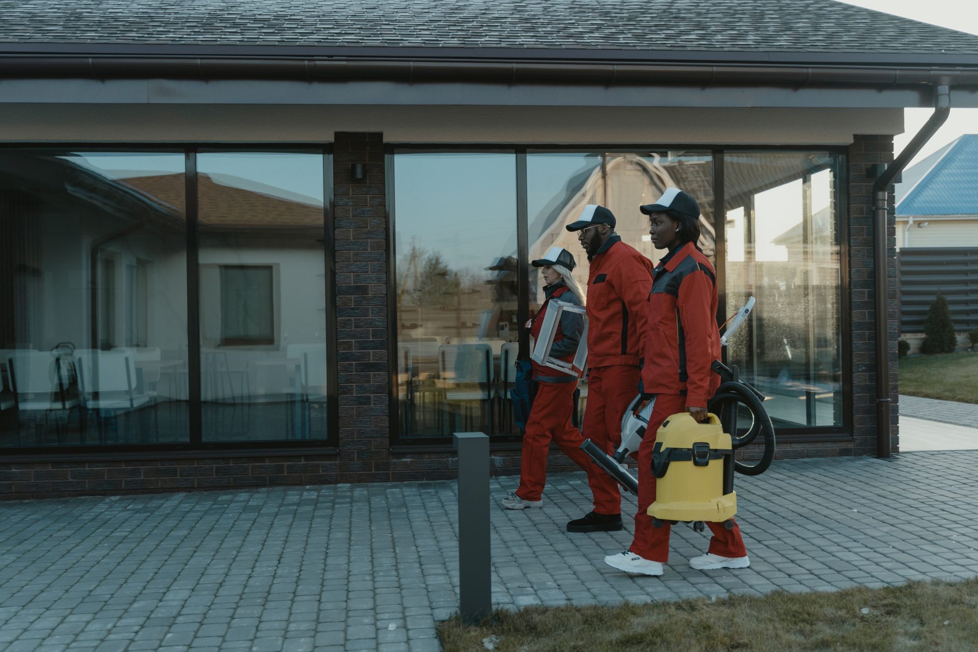 Ein professionelles Reinigungsteam in Uniformen nähert sich mit Ausrüstung einem Haus mit Glasfassade.